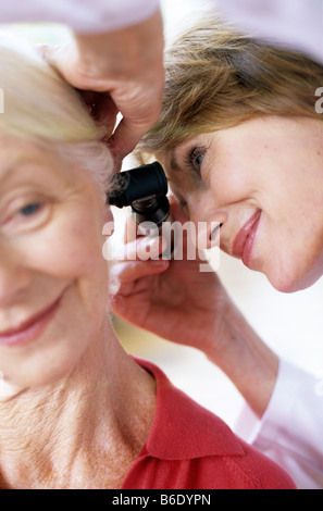 Esame dell'orecchio. Pratica generale medico esaminando un 63-anno-vecchia donna l orecchio utilizzando un otoscopio. Foto Stock