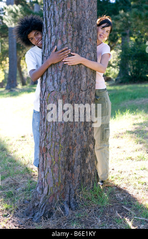 Tree avvolgente. Giovane donna e uomo con le loro braccia attorno ad un tronco di albero. Foto Stock