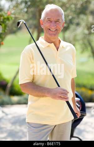 Giocatore di golf. Uomo in possesso di un golf club e tirando la sua sacca da golf su un carrello. Foto Stock