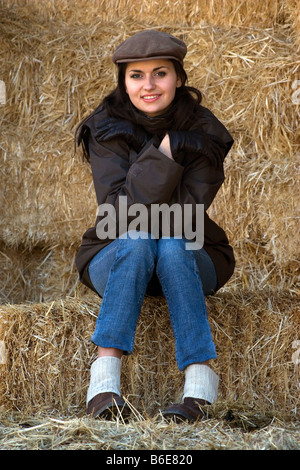 Ritratto di giovane moderno donna seduta nel fienile dresssed in marrone impermeabile e cappuccio di velluto a coste Foto Stock