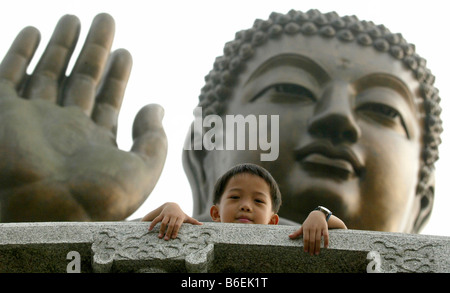 Ragazzo nella parte anteriore di un buddha di bronzo al Monastero Po Lin, Isola di Lantau, villaggio di pescatori, Hong Kong, Cina, Asia Foto Stock