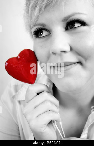 Giovane donna tenendo un cuore contro il suo controllo con un sguardo amoroso sul suo viso Foto Stock