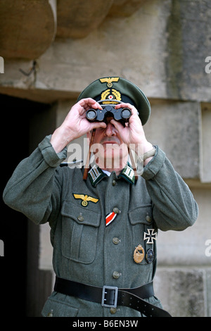 Un attore vestito come un ufficiale tedesco soldato che si affaccia sul canale in lingua inglese e da un tedesco D giorno bunker in Normandia Francia Foto Stock