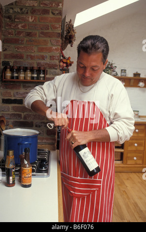 Uomo di mezza età per la cottura in cucina di paese di aprire una bottiglia di vino Foto Stock