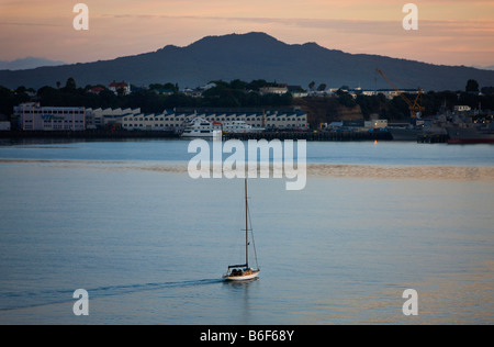 Una imbarcazione a vela testa fuori all'alba nel porto di Waitemata, con Rangitoto Island in background, Auckland, Nuova Zelanda. Foto Stock