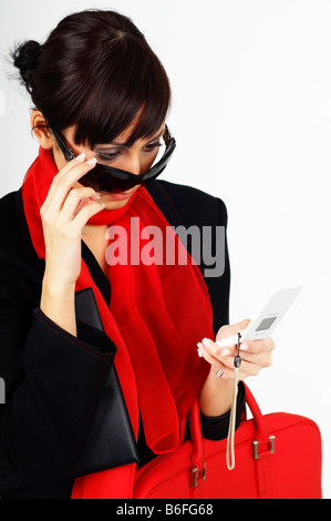 Azienda giovane donna che indossa gli occhiali da sole, guardando il suo telefono cellulare Foto Stock