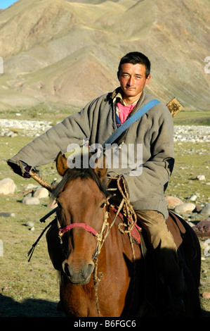 Il nomade, giovane uomo che indossa un costume tradizionale con un fucile seduto sul suo cavallo nella steppa, Kharkhiraa, mongola Altai nea Foto Stock