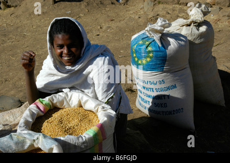 La fame, la ragazza sorridente accanto ai sacchi di grano di sorgo donato dall'UE, sbarcare mercato, Etiopia, Africa Foto Stock