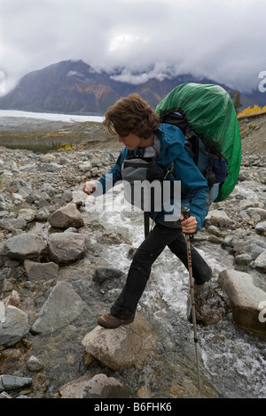 Escursionista, backpacker, attraversando creek, donna Donjek percorso, St. Elias montagne, Parco Nazionale Kluane, Yukon Territory, Canada, né Foto Stock