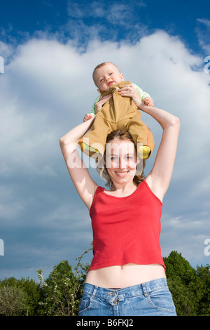 Giovane e bella madre, 25 anni, con il suo figlio, 7 mesi, sul suo capo, esterno Foto Stock