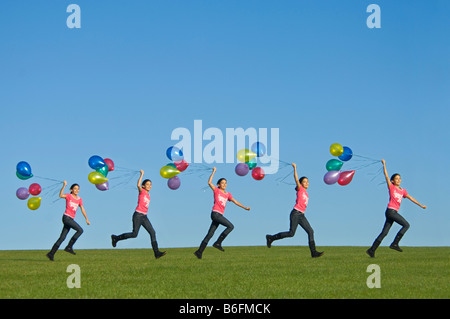 Una sequenza di immagini di una giovane ragazza (11) acceso felicemente in tutta l'erba verde con un mucchio di palloncini arrancano dietro e cielo blu. Foto Stock