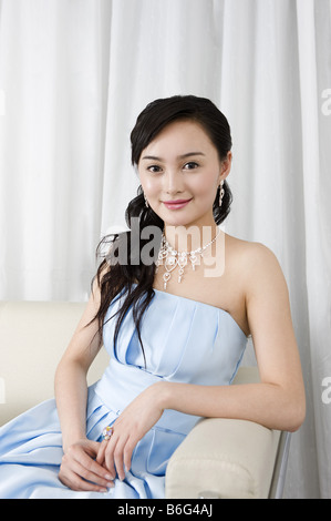 Sorridente giovane donna che indossa un vestito blu vestito seduto sul divano Foto Stock