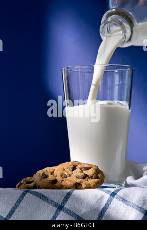 Vetro e bottiglia di latte con i cookie su uno sfondo blu con latte di colata Foto Stock