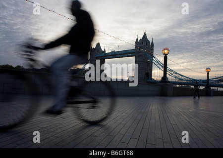 Alla prima luce, un inizio di mattina ciclista passa di Tower Bridge sulla riva sud del fiume Tamigi a Londra Foto Stock