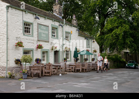 L'esterno del Fountaine Inn (attraente pub di campagna dipinto di bianco, posti a sedere all'esterno e 2 escursionisti in arrivo) - Linton, North Yorkshire, Inghilterra, Regno Unito Foto Stock