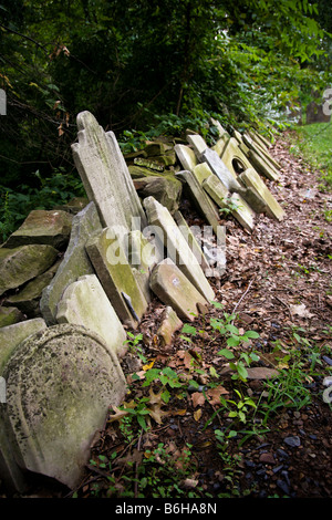 Vecchio scartato , usura e rotture di lapidi impilate contro un muro di pietra ricoperta da fitta vegetazione lussureggiante. Foto Stock