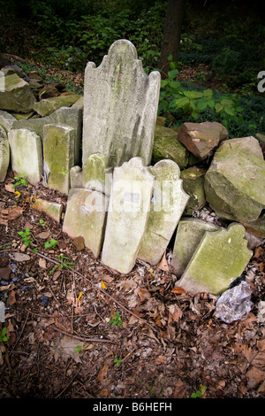 Vecchio scartato , usura e rotture di lapidi impilate contro un muro di pietra ricoperta da fitta vegetazione lussureggiante e foglie. Foto Stock