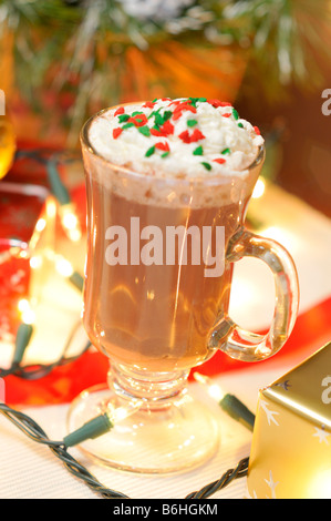 Vacanza festosa scena della tazza di cioccolata calda con panna montata e rabboccato con colorati irrora con presenta nella parte anteriore dell'albero di natale. Foto Stock