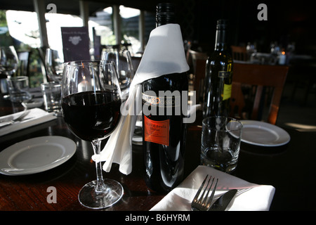 Un elegante bottiglia di vino rosso in un bicchiere e in una bottiglia su un tavolo in un ristorante. la bottiglia di vino rosso ha un tovagliolo bianco Foto Stock