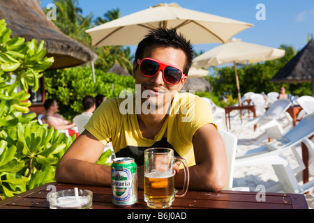 Un giovane uomo seduto al tavolino di un bar sulla spiaggia alle Maldive (Thulhagiri Island) Foto Stock