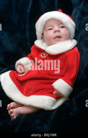 Tre mesi di età bambina vestito in un abito di Santa e cappello di Natale per contro uno sfondo scuro Foto Stock