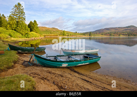 Riflessione a telecomando Loch Ordie, nr Dunkeld, Scozia, preso poco dopo l'alba con tre vecchie imbarcazioni a remi in primo piano Foto Stock