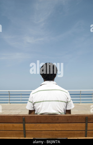 Uomo seduto su un banco in riva al mare Foto Stock