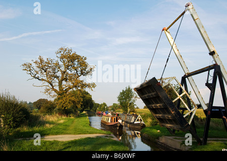Inghilterra, Shropshire, Whitchurch. Una chiatta passa sotto un ponte cantiliver su un tratto tranquillo della Shropshire Union Canal. Foto Stock