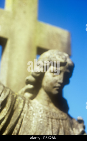 Impressionistica dettaglio di calcare pietra tombale angelo testa e spalle in luce calda con pietra grande crocifisso dietro Foto Stock