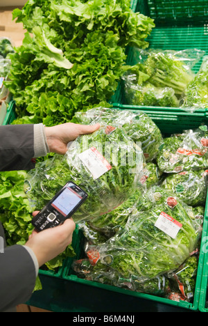 Giovane donna analizza il prezzo di un insalata confezionato nel suo telefono cellulare nel futuro reale di memorizzare una parte di Metro Group Foto Stock