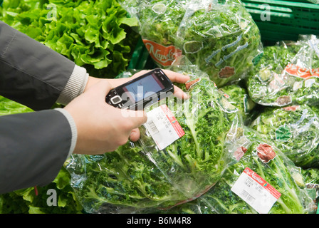 Giovane donna analizza il prezzo di un insalata confezionato nel suo telefono cellulare nel futuro reale di memorizzare una parte di Metro Group Foto Stock
