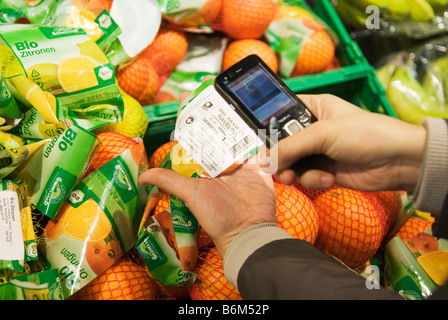 Giovane donna scansiona il prezzo di pacchetti di frutta nel suo telefono cellulare in un supermercato Foto Stock