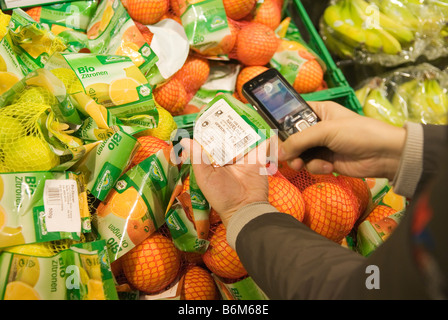 Giovane donna scansiona il prezzo di pacchetti di frutta nel suo telefono cellulare nel futuro reale di memorizzare una parte di Metro Group Foto Stock