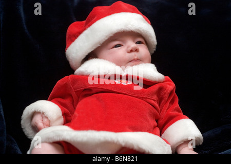 Tre mesi di età bambina vestito in un abito di Santa e cappello di Natale per contro uno sfondo scuro Foto Stock