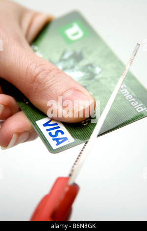 Concetto di mano in possesso di una carta di credito visa mentre le forbici taglia fino che simboleggiano tempi di magra Foto Stock