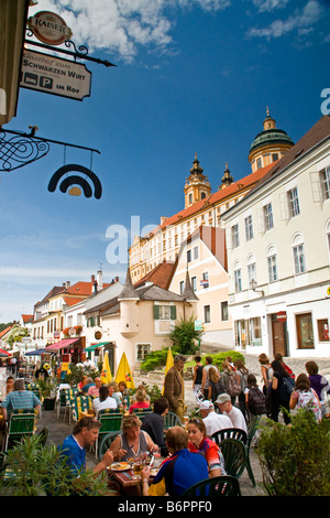 L'Abbazia di Melk incombente sull turisti in outdoor cafe nella città di Melk al di sotto, nella pittoresca valle di Wachau lungo il Fiume Danubio Foto Stock