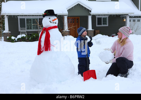 La madre e il giovane ragazzo a giocare nella neve con pupazzo di neve e casa Foto Stock