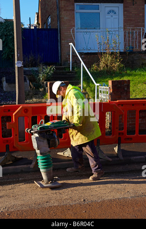 Workman utilizzando per impieghi pesanti pounder per libbra di ghiaia in strada dopo la posa dei cavi elettrici Foto Stock