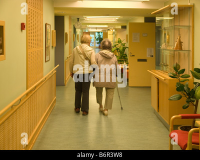 Donna middleaged aiutando la madre a piedi nel corridoio di una casa di riposo per anziani Foto Stock