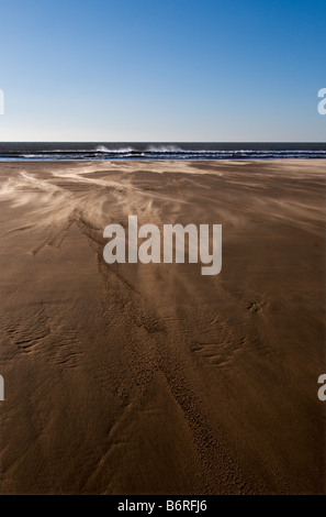 Il vento soffia sabbia attraverso la spiaggia vuota a Dunraven Bay nel Galles del Sud. Foto Stock