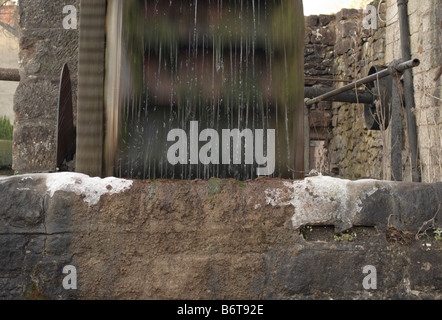 Un lavoro ruota di acqua su un freddo inverno mattina nel Derbyshire con il gocciolamento di acqua spray di congelamento sul muro di pietra Foto Stock