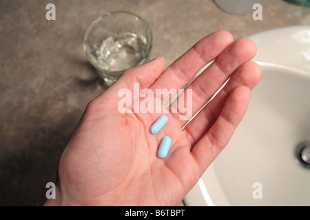 Uomo di mezza età la mano che regge due pillole blu in scena da bagno Foto Stock