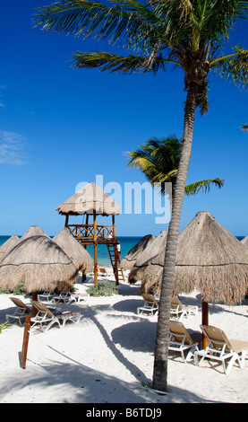 Playa Mujeres Beach ombrelloni e sedie Messico // PLAYA MUJERES, Messico - sedie da spiaggia e ombrelloni di paglia sono disposti sulla spiaggia di sabbia bianca di Playa Mujeres al sole. Questa destinazione turistica si trova sulla costa nord-orientale della penisola dello Yucatan, a circa 10 chilometri (6 miglia) a nord di Cancun. Playa Mujeres è conosciuta per le sue spiagge incontaminate e gli edifici di lusso che hanno trasformato questa zona costiera in una popolare destinazione turistica. La spiaggia fa parte della più ampia regione della Riviera Maya, che si estende lungo la costa caraibica del Messico. La zona si trova Foto Stock