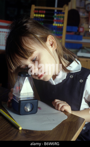 Bambina in una scuola primaria che studiano in aula un insetto utilizzando una casella di ingrandimento Foto Stock