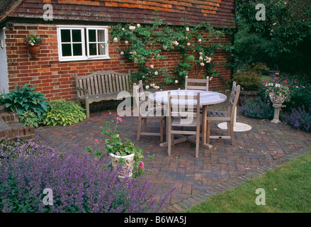 Tavolo in legno e sedie in mattoni a spina di pesce patio pavimentato in parte anteriore del mattone cottage di campagna in estate Foto Stock