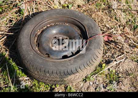 Una vecchia auto abbandonate la ruota e il pneumatico oggetto di dumping dal lato della strada. Foto Stock