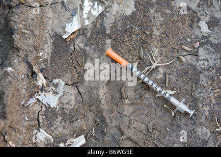 Un ago ipodermico lasciato in posa sul terreno in una città interna slum. Foto Stock