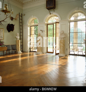 Busti classici su plinti in marmo nel grande paese vuoto hall con un pavimento in parquet lucido e arcuata di porte Francesi Foto Stock