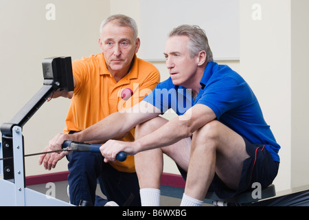 Personal trainer aiutando un uomo su un vogatore Foto Stock