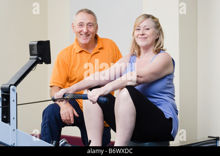 Personal trainer aiutando una donna su un vogatore Foto Stock